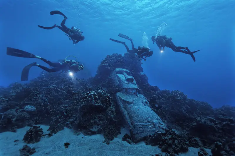 Underwater Moai. Basic Info: Easter Island is the most remote inhabited island in the world. The nearest population center is Chile (2300 miles) and the nearest Polynesian center in the opposite direction is Tahiti (2600 miles). Easter Island, (Rapa Nui, Isla de Pascua) is famous for Moai everywhere along the coast toppled on their AhuÕs and littered abandoned in the center along the Moai roads used to transport them. Polynesians had a knack for colonizing even the most inhospitable oceanic rock. They were adept sailors, explorers, colonizers and their experience taught them the best way to escape war or famine was to sail east, to windward in search of new islands. There is no evidence that a 2nd group reached the island in early history as Heyerdall alledges Ð in fact it points to the opposite. Easter Island had military rule until 1965 and had cashless societies of fishing and farming that have since been broken apart by independence and a dependence on tourism. Rapanui incest laws are strict with everybody tracing roots to 30 or so couples who survived 19th century Peruvian slave raiding and epidemics. Legal romance was at an impasse so mixed marriages now abound on the island.