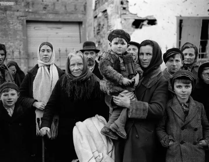 Grim-faced refugees stand in a group on a street in La Gleize, Belgium on Jan. 2, 1945. They are waiting to be transported from the war-torn town after its recapture by American forces during the German thrust into the Belgium-Luxembourg salient. (AP Photo/Peter J. Carroll)